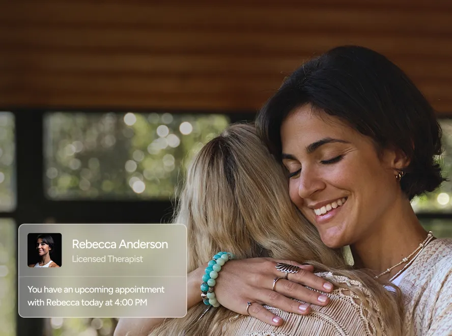 Two women hugging with a softly smiling expression, overlaid with a notification showing therapist Rebecca Anderson and an appointment at 4:00 PM.